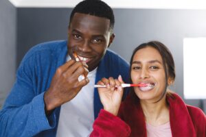 Happy diverse couple in brushing teeth in bathroom, looking to camera smiling. Happiness, domestic life, self care and inclusivity concept. Happy diverse couple in brushing teeth in bathroom, looking to camera smiling. Happiness, domestic life, self care and inclusivity concept.